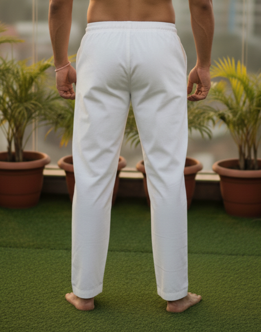 Man standing on a rooftop with a cityscape view, wearing white pants.