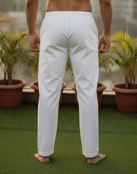 Man standing on a rooftop with a cityscape view, wearing white pants.