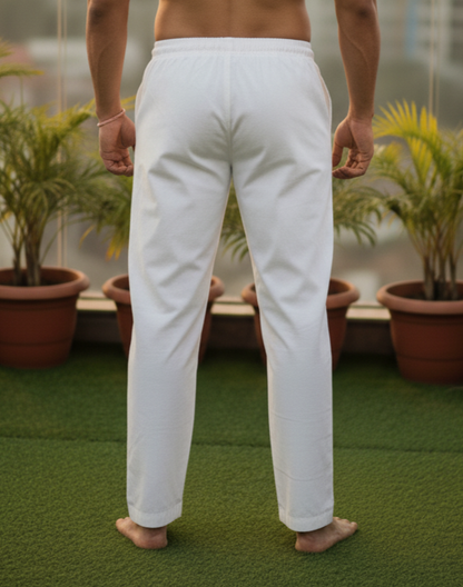 Man standing on a rooftop with a cityscape view, wearing white pants.